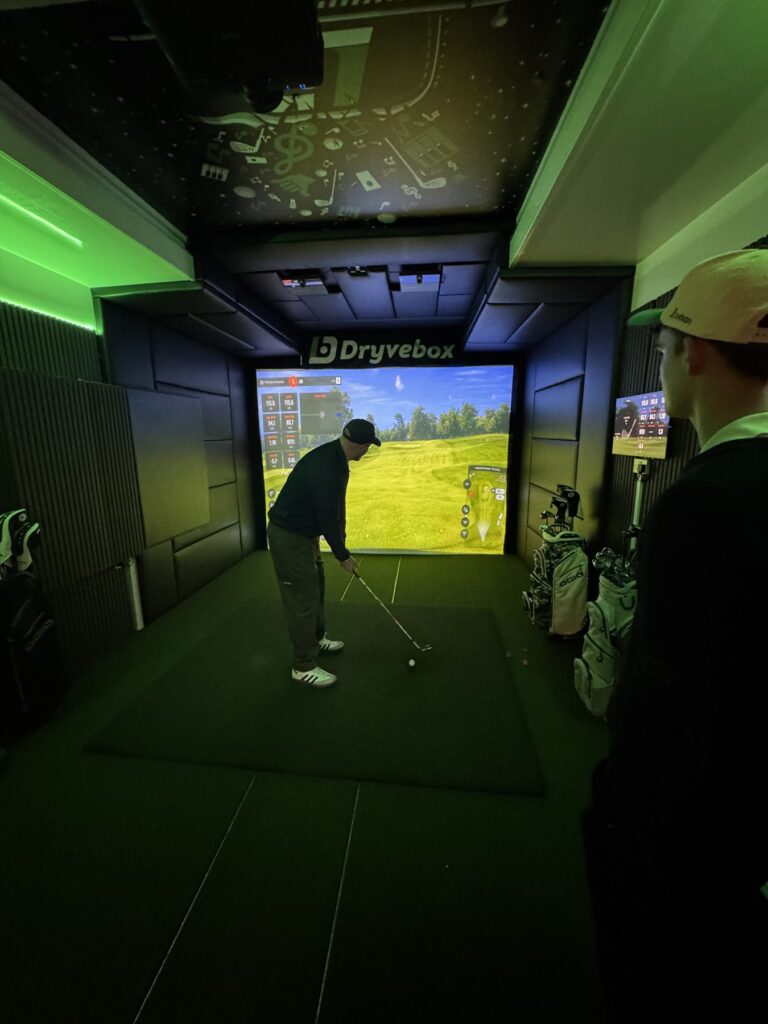 Interior of the Dryvebox golf simulator lit with green LED lighting as a golfer takes a shot
